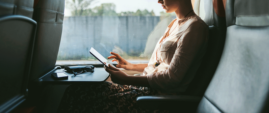 A person travelling on a train, looks at a tablet.