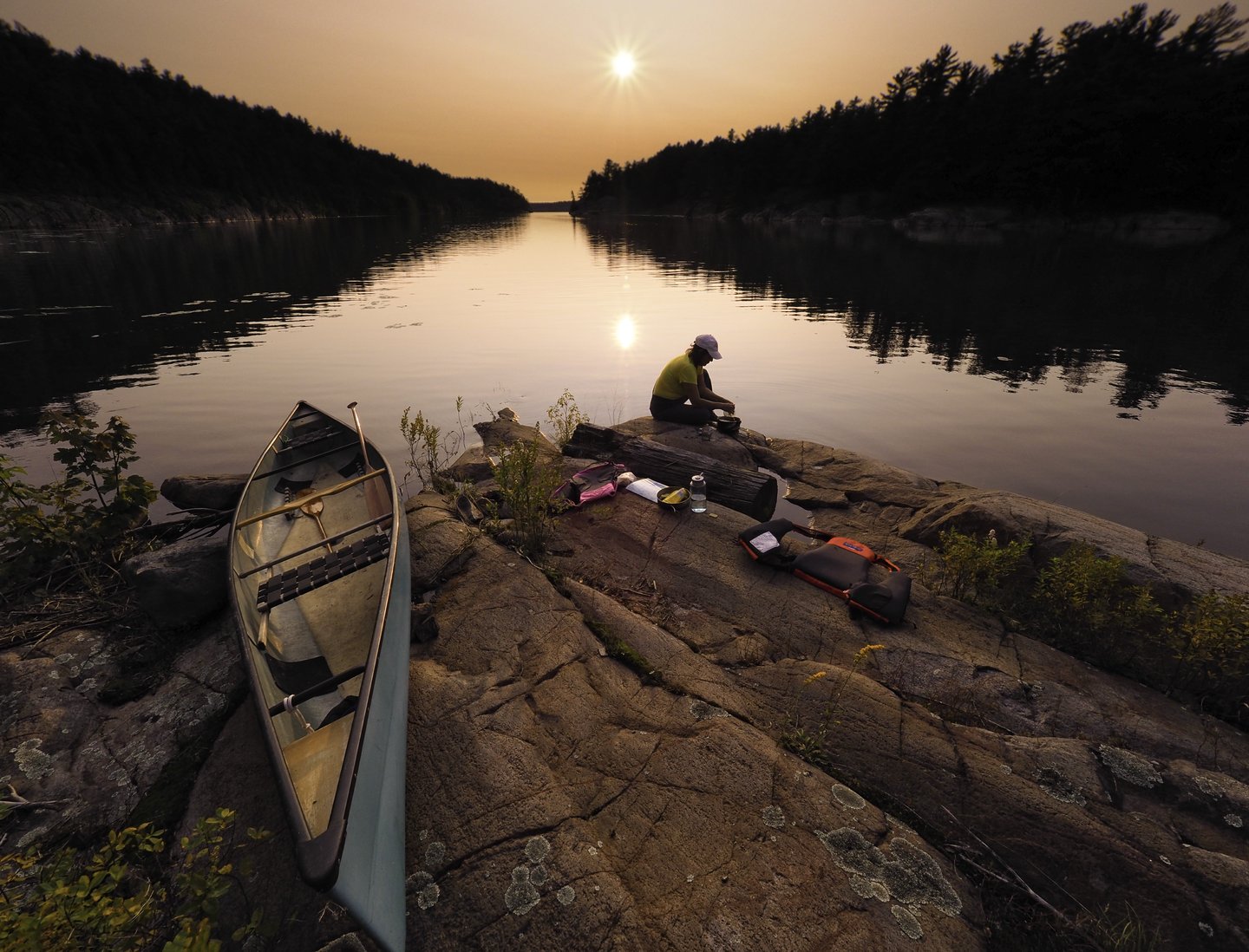 A person sitting on a rocky shore with a canoe.