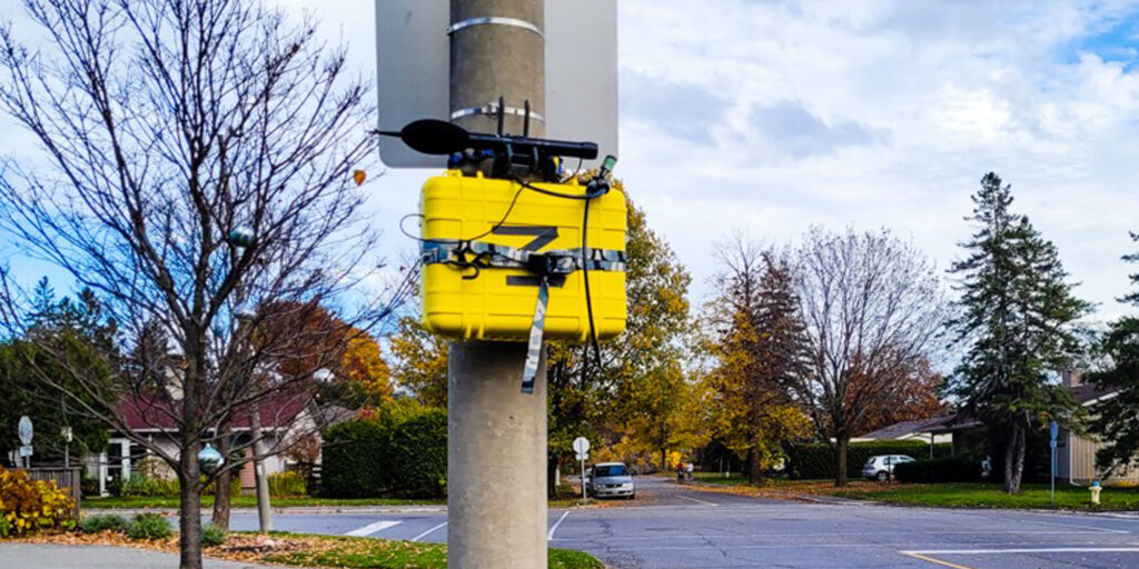 A pole with a yellow monitoring box on it.