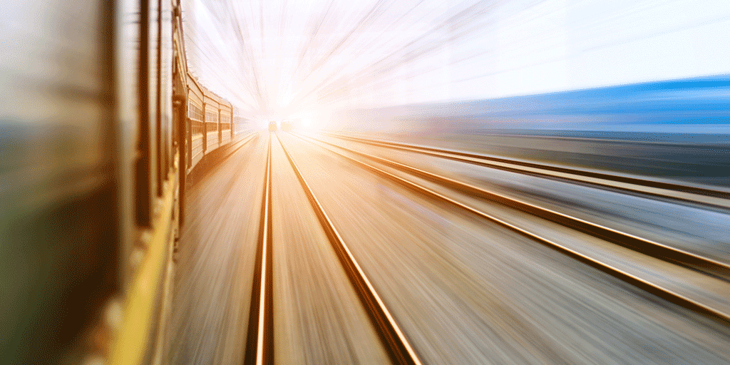 Train tracks leading towards the horizon with overhead wires and a train passing quickly.
