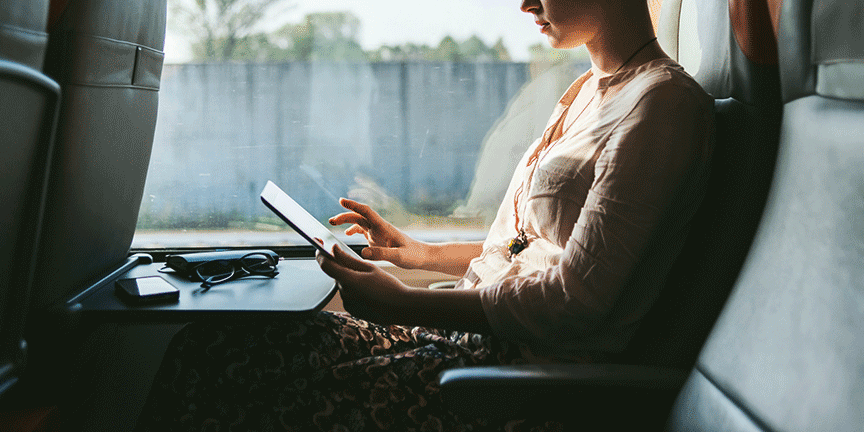 A person travelling on a train, looks at a tablet.