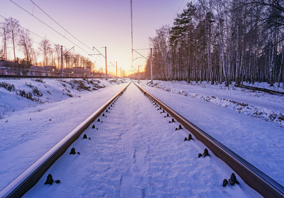 Train tracks covered in snow and overhead electrical wires, facing towards the horizon.